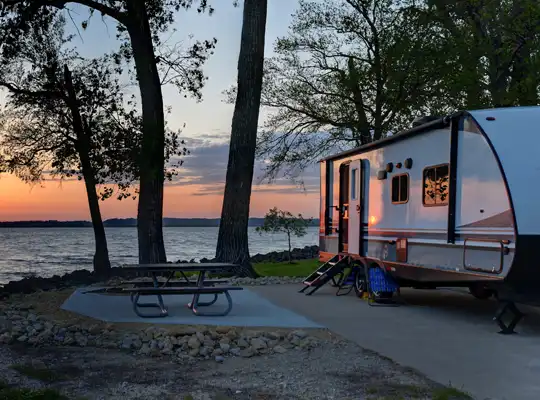 camp trailer near a lake at sunset